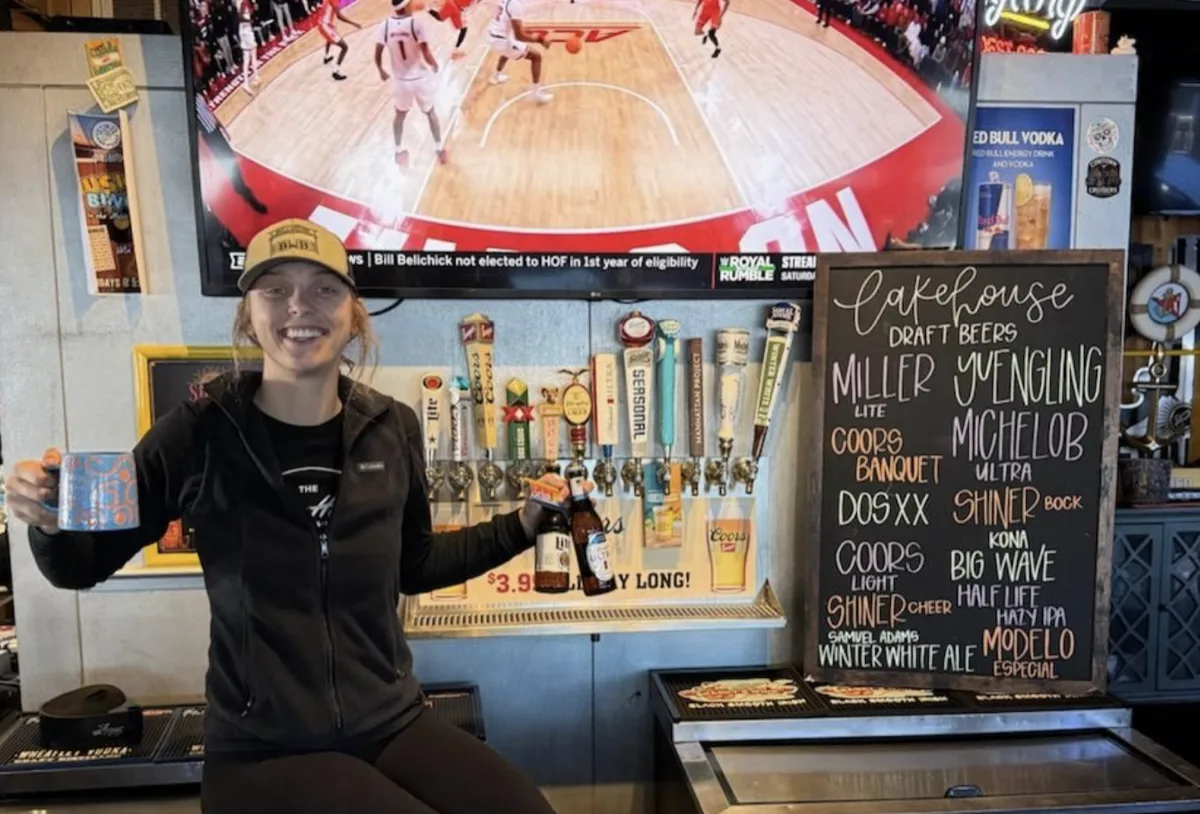 A Lakehouse bartender behind the bar with draft beer taps and the house chalkboard beer list