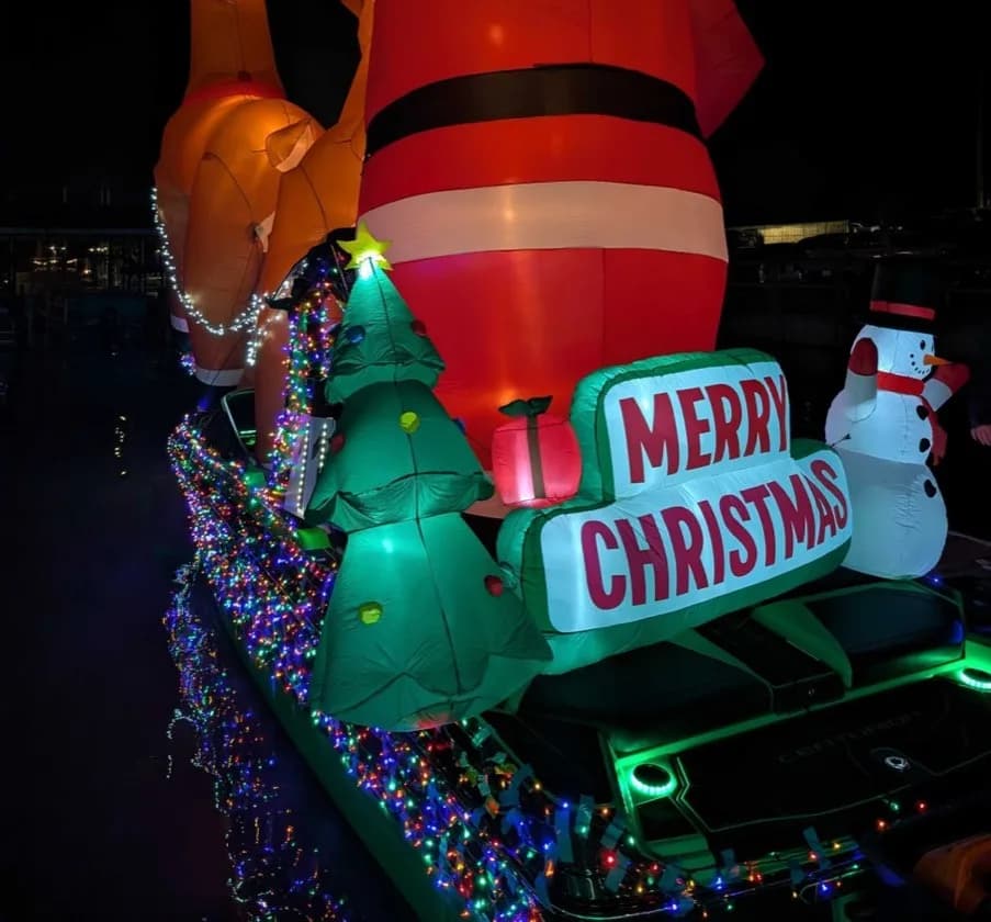 The Lakehouse Merry Christmas parade boat — inflatable Santa, Christmas trees, snowman, and Merry Christmas sign wrapped in lights
